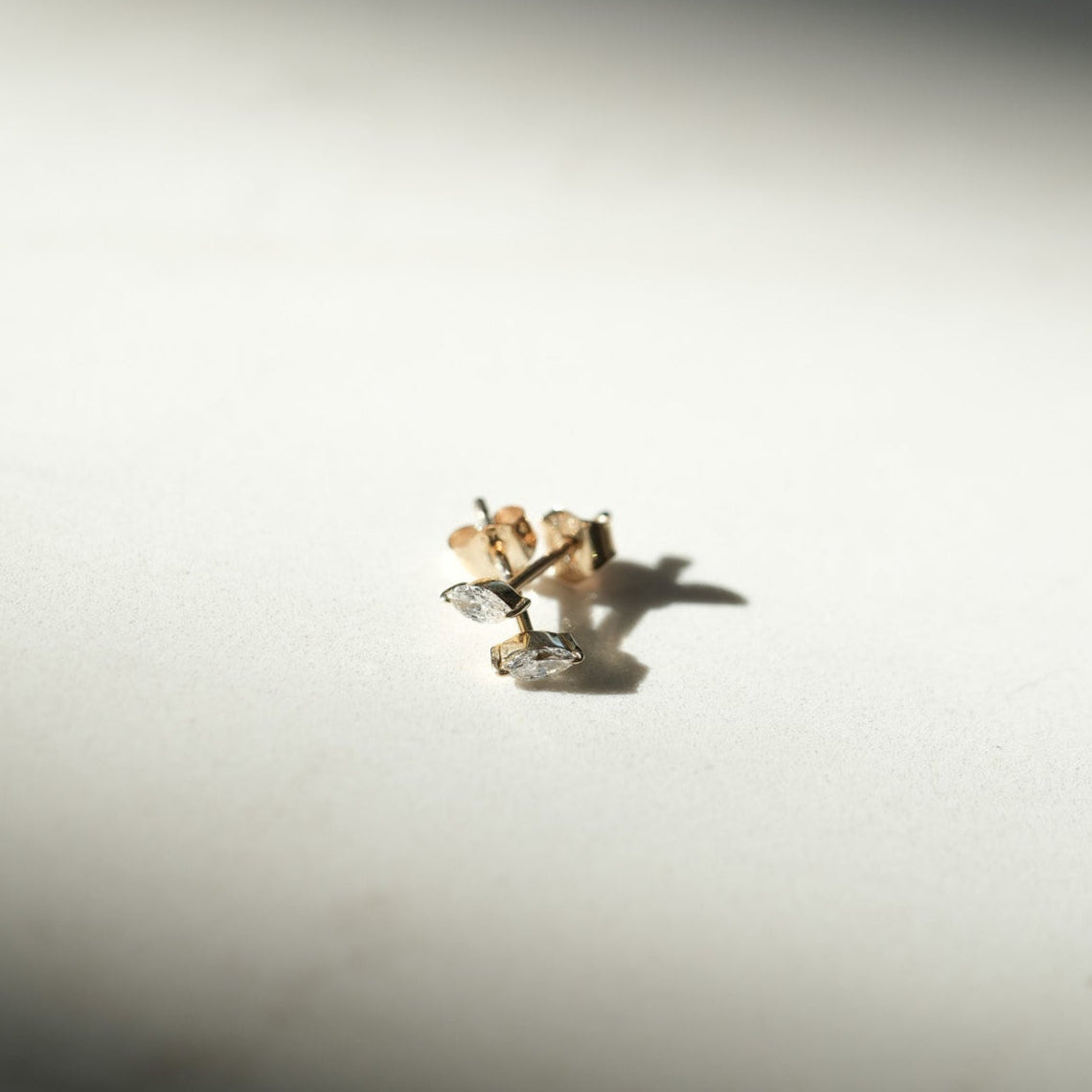 Small gold earring on a light surface with shadows