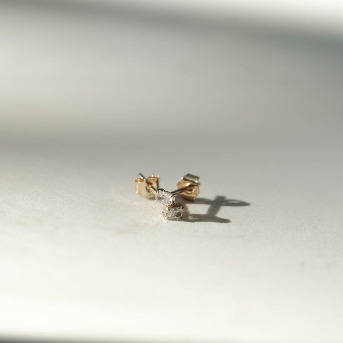Gold earring on a white surface with soft shadows