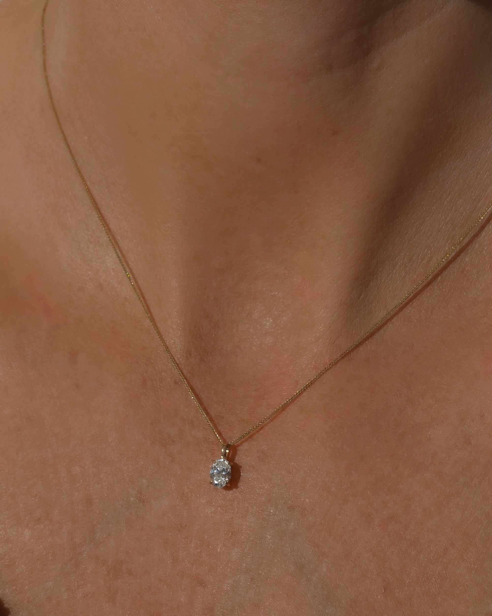 Gold necklace with a small oval diamond pendant on a person's neck